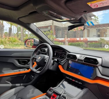 Modern interior of a Lamborghini Urus featuring black leather and orange accents with a digital cockpit.