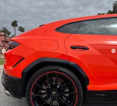 Side profile of a bright orange Lamborghini Urus luxury SUV with black rims and red accents.