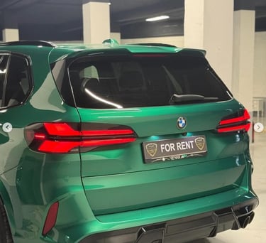 Rear view of a metallic green BMW X5 luxury SUV for rent in an indoor parking garage.