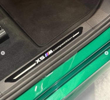 Close-up of a BMW X5 M Competition door sill plate with the M logo on a green luxury SUV.