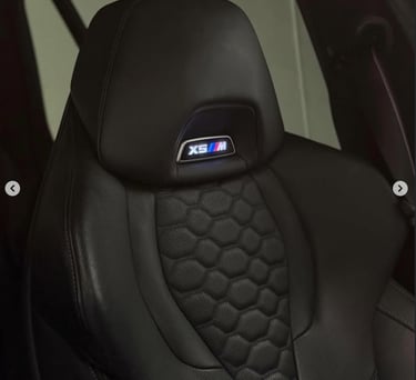 Close-up of a black leather BMW X5M sport seat with quilted hexagonal pattern and illuminated M badge logo.