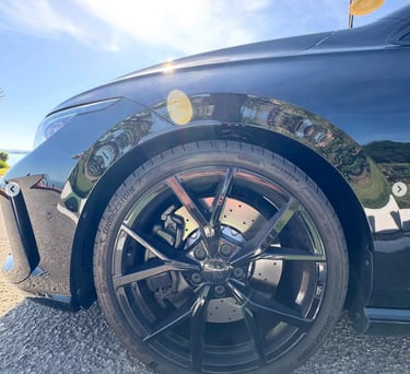 Close-up of a black sports car wheel featuring Bridgestone Potenza tires and gloss black alloy rims.