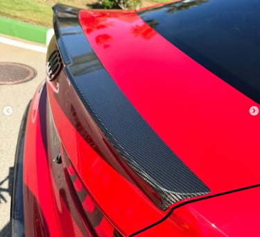 A red Audi sedan featuring a custom carbon fiber trunk spoiler for enhanced vehicle aerodynamics.