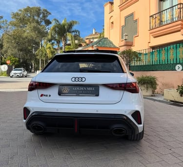 Rear view of a white Audi RS3 sportback luxury car rental parked in front of a villa.