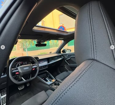 Interior view of an Audi luxury car with black leather seats and an open panoramic sunroof.