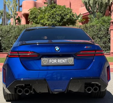 Rear view of a blue BMW M5 luxury rental car parked in front of a Mediterranean villa.