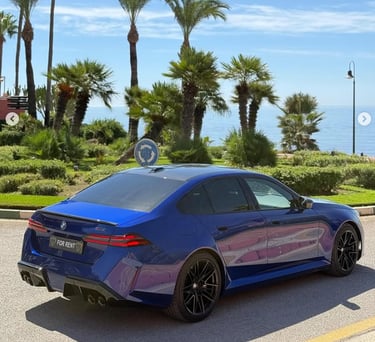 A blue BMW M5 luxury sedan for rent parked near tropical palm trees and a scenic ocean coastline.