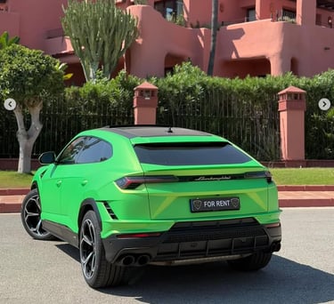 A bright green Lamborghini Urus luxury SUV for rent parked in front of a pink Mediterranean style building.