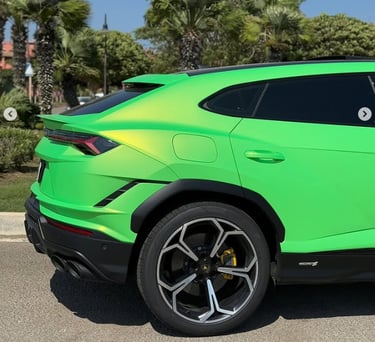 Side view of a bright lime green Lamborghini Urus SUV parked outdoors near tropical palm trees.