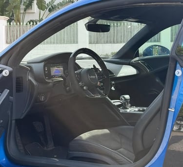 Interior view of a blue Audi R8 sports car showing the black leather seats and luxury dashboard.