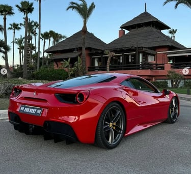 Red Ferrari 488 luxury sports car parked in front of a tropical resort with palm trees.