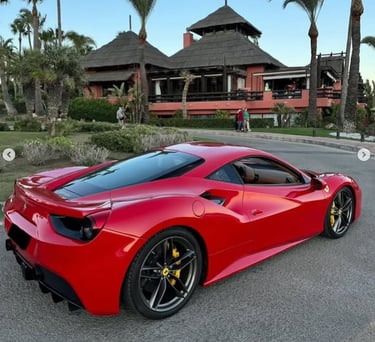 Red Ferrari 488 GTB luxury sports car parked in front of a tropical resort with palm trees.