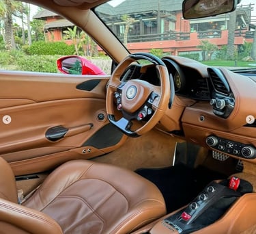 Luxury Ferrari interior with tan leather seats and carbon fiber trim on the dashboard and steering wheel.