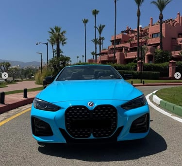 Front view of a bright blue BMW convertible parked on a tropical road with palm trees.