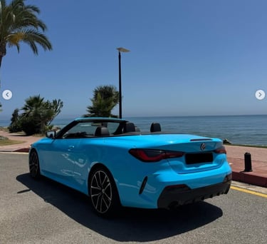 A bright blue convertible BMW parked on a coastal road with palm trees and a view of the ocean.