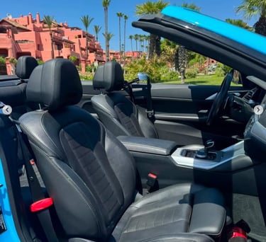 Luxury blue convertible interior with black leather seats parked near tropical palm trees.