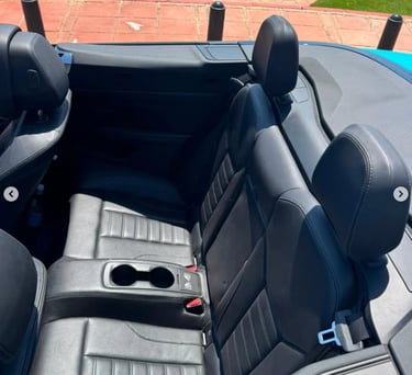 Rear black leather seats and cup holders in a luxury convertible car parked near the coast.
