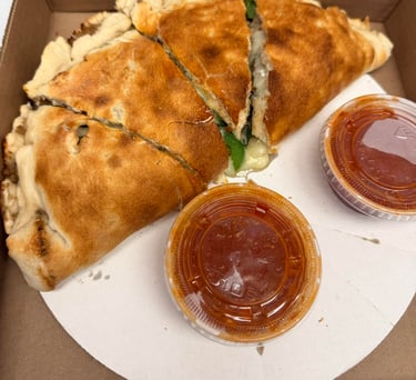 Golden brown sliced cheese calzone in a delivery box with two sides of red marinara sauce.