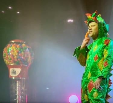 Piff the magic dragon stands on stage next to a giant lumball machine.