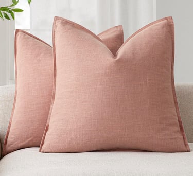 Set of dusty rose linen throw pillows with flanged edges arranged on a light-colored sofa.