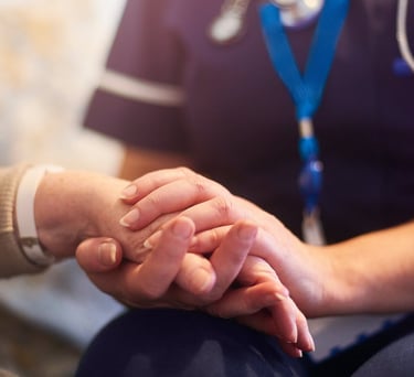 A healthcare nurse in blue scrubs holding an elderly patient's hand to provide comfort and support.