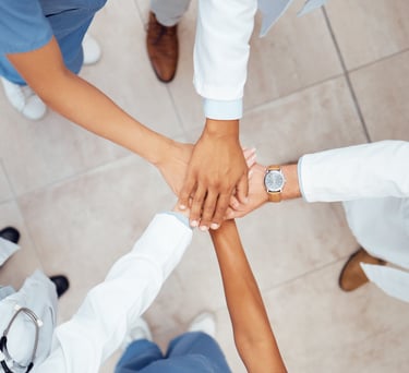 A diverse medical team of doctors and nurses joining hands in a huddle for healthcare collaboration.