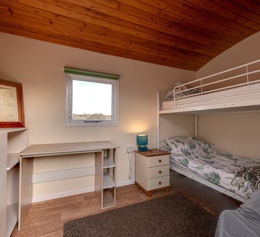 Bedroom with bunk beds, a study desk, and wood paneling on the ceiling.