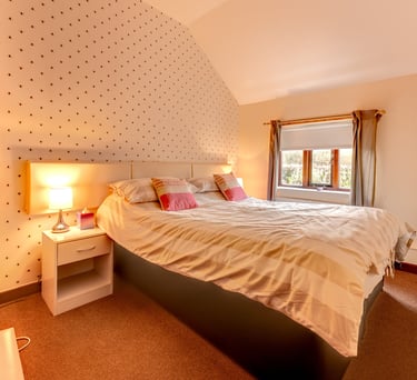 Cozy modern bedroom with a striped duvet, warm lamp lighting, and patterned wallpaper.