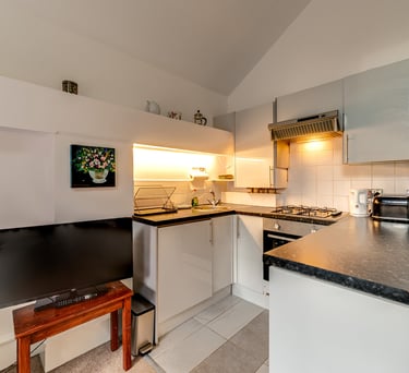 Modern studio apartment kitchen with white cabinets, dark countertops, and integrated appliances.