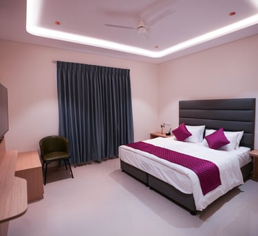 Modern hotel room with king-size bed, purple pillows, and recessed ceiling lighting.