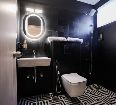 Modern luxury bathroom with black tile walls, illuminated oval mirror, and geometric floor tiles.