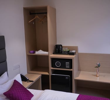 Modern hotel room interior featuring a wooden open wardrobe with safe, mini fridge, and coffee station.