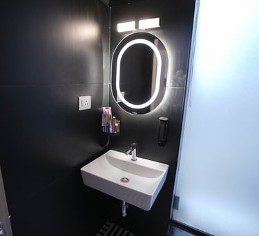 Modern bathroom featuring a white ceramic sink and an illuminated oval LED mirror against black walls.
