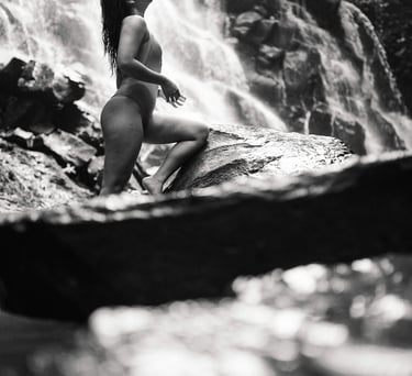 Black and white portrait of woman standing near waterfall rocks at Kanto Lampo Bali