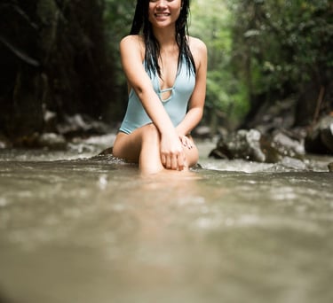 Woman sitting in shallow water during portrait session at Kanto Lampo Waterfall Bali