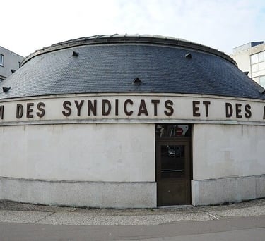 Photo de la Maison des Syndicats entourée de bâtiments, avec un bâtiment rond surnommé la Petite Rotonde