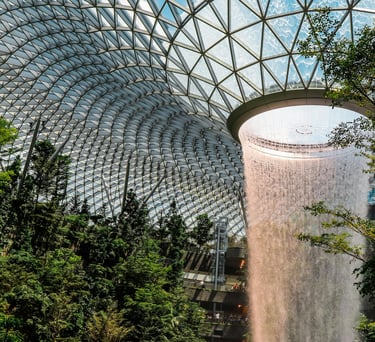 Indoor waterfall under a glass dome with lush greenery.