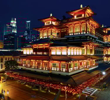 Buddha Tooth Relic Temple in Singapore Chinatown illuminated at night with modern city skyline in the background