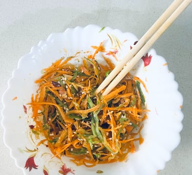 Fresh carrot and green pepper slaw with sesame seeds in a white bowl with wooden chopsticks.