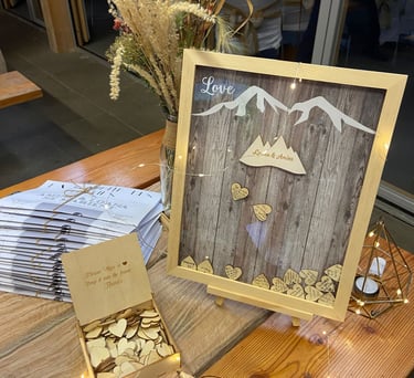 Rustic wedding guest book display featuring a mountain shadow box frame with wooden heart tokens.