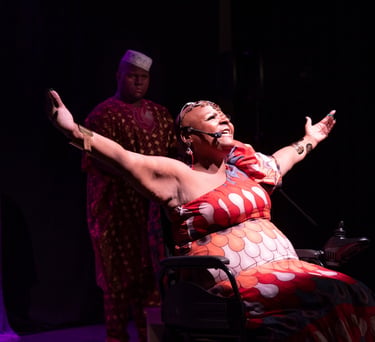 Fotografia de cena teatral com a artista Mona Rikumbi. Mulher negra, usuária de cadeira de rodas