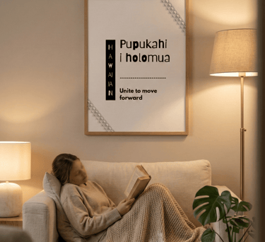 “Kulia i ka nuʻu” Hawaiian wall art above sofa in cozy evening living room with woman reading.