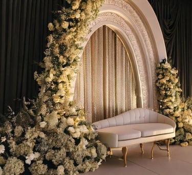 Elegant wedding stage in dubai decor with a white sofa, ornate arch, white floral arrangements.