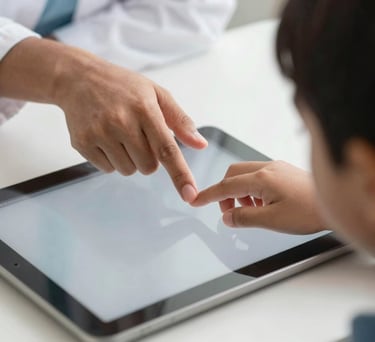 Close-up of a child's hand using an iPad for a communication therapy session, with a South Asian therapist's hand guiding gently in a focused, evidence-based setting.