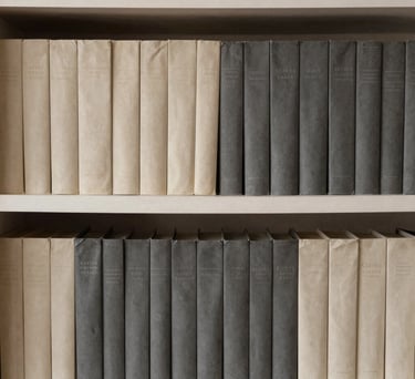 A close-up of a shelf filled with books, organized by color in shades of cream and charcoal grey. Minimalist home library in a South American residence.