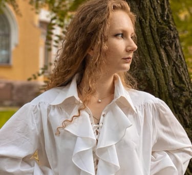 A woman with red-blonde hair wearing a white poet shirt, with a large collar and ruffled front.