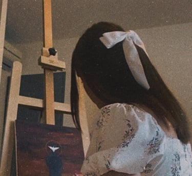 Une jeune femme dans une robe blanche avec un noeud blanc dans les cheveux en train de peindre