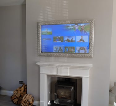 Bespoke Samsung TV installation above a fireplace featuring a custom-made frame and mirror glass
