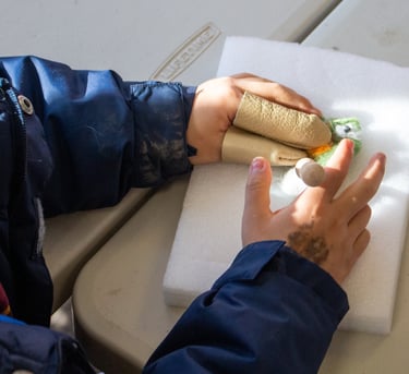 Young child's hands with finger coverings, poking pieces of wool to create a felted creature.