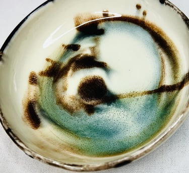 A glazed plate with black lid and abstract brown and green spots and shades